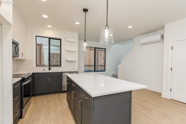 kitchen with appliances with stainless steel finishes, a wall mounted air conditioner, a kitchen island, decorative light fixtures, and light hardwood / wood-style flooring