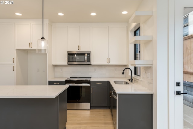 kitchen with appliances with stainless steel finishes, sink, pendant lighting, white cabinets, and light stone counters