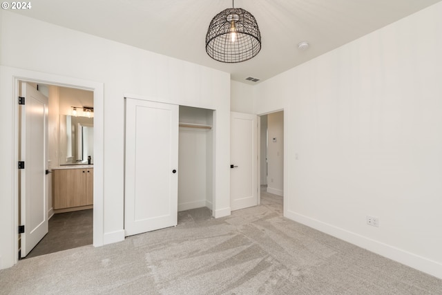 unfurnished bedroom with light carpet, a closet, and ensuite bath