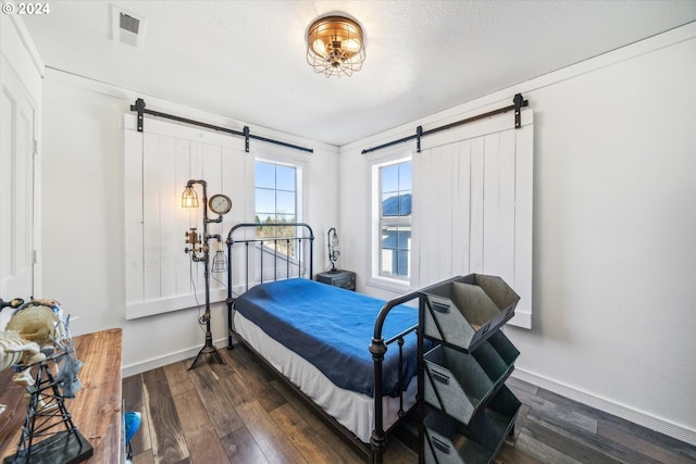 bedroom with a barn door, dark hardwood / wood-style flooring, ornamental molding, and a textured ceiling