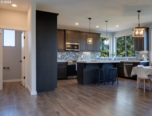 kitchen with backsplash, hanging light fixtures, a kitchen island, dark hardwood / wood-style flooring, and stainless steel appliances