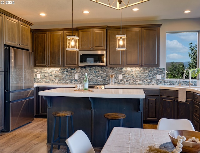 kitchen with pendant lighting, light hardwood / wood-style flooring, appliances with stainless steel finishes, tasteful backsplash, and a breakfast bar area