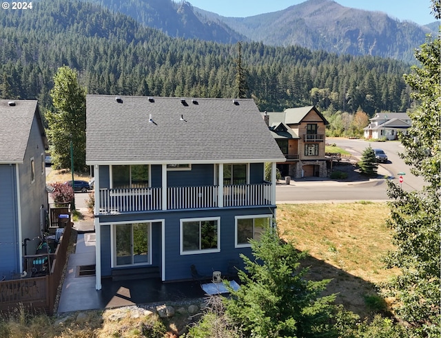 back of property with a mountain view, a balcony, and a patio