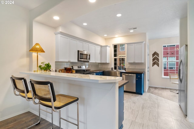 kitchen with a breakfast bar, a peninsula, white cabinets, and appliances with stainless steel finishes
