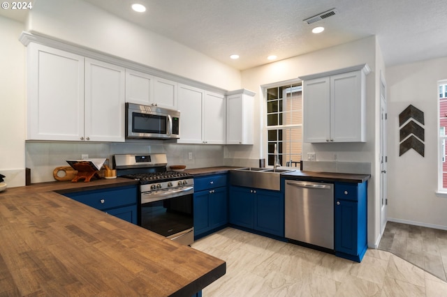 kitchen with blue cabinets, visible vents, a sink, appliances with stainless steel finishes, and butcher block counters
