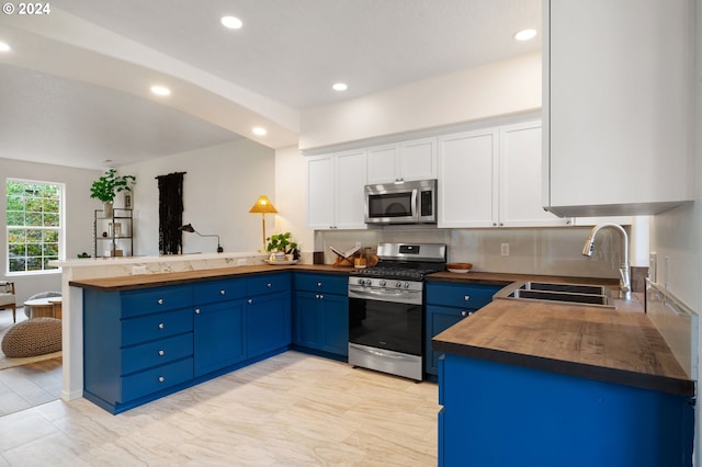 kitchen with wooden counters, a peninsula, blue cabinetry, a sink, and appliances with stainless steel finishes