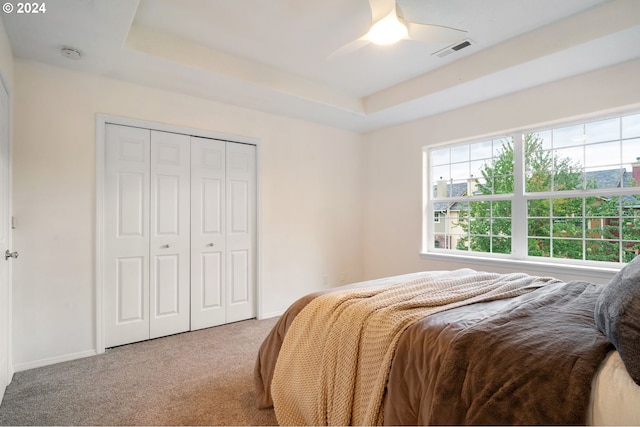 bedroom featuring a closet, ceiling fan, a raised ceiling, and light carpet