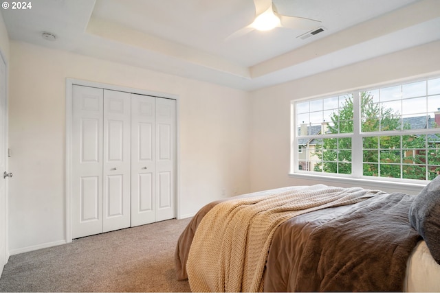 bedroom with carpet, visible vents, baseboards, a tray ceiling, and a closet