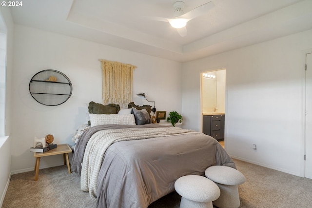 bedroom with a tray ceiling, light carpet, baseboards, and ensuite bathroom