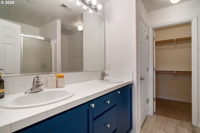 bathroom featuring a textured ceiling, a shower stall, visible vents, and a sink