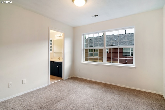 unfurnished bedroom featuring visible vents, baseboards, a sink, ensuite bathroom, and light colored carpet