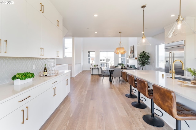 kitchen featuring a kitchen bar, sink, hanging light fixtures, stainless steel built in fridge, and white cabinets