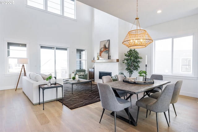 dining space with a fireplace, a towering ceiling, plenty of natural light, and light hardwood / wood-style floors