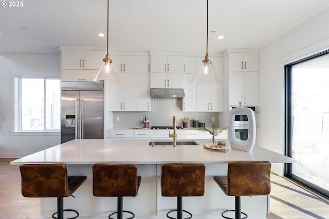 kitchen with plenty of natural light, a kitchen island with sink, built in fridge, and white cabinets