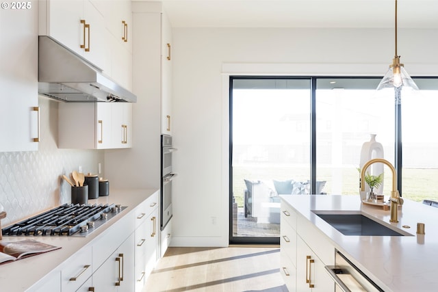 kitchen featuring tasteful backsplash, sink, white cabinets, and decorative light fixtures