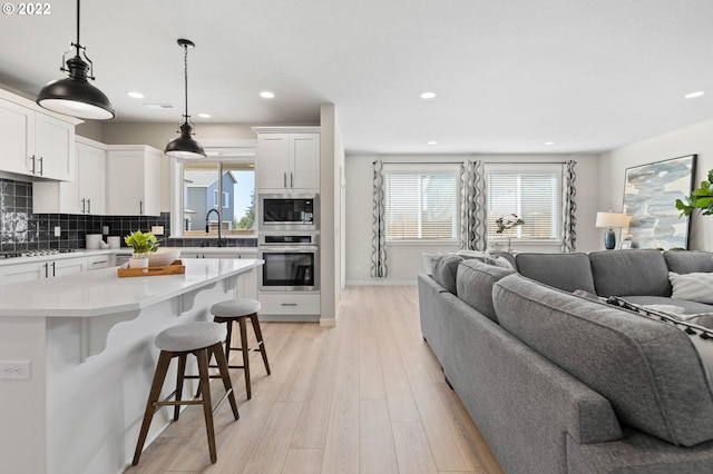 kitchen with appliances with stainless steel finishes, white cabinetry, pendant lighting, a breakfast bar, and backsplash