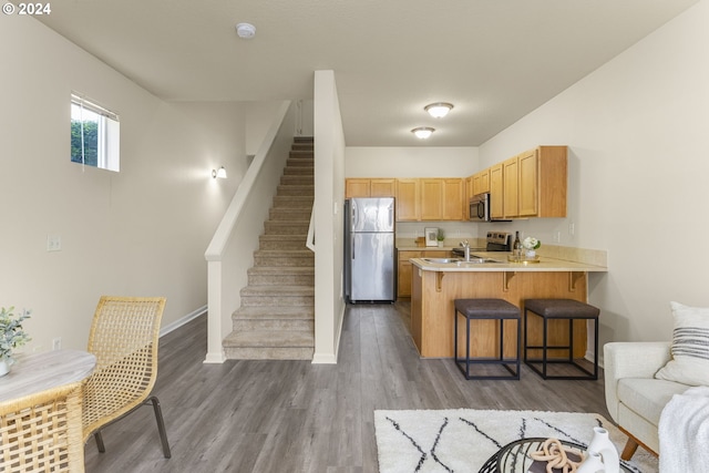 kitchen featuring appliances with stainless steel finishes, dark hardwood / wood-style floors, a kitchen bar, light brown cabinetry, and kitchen peninsula