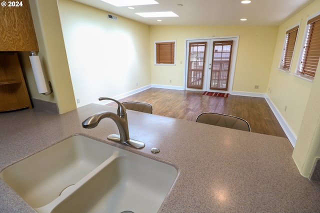 kitchen featuring wood-type flooring, lofted ceiling with skylight, french doors, and sink