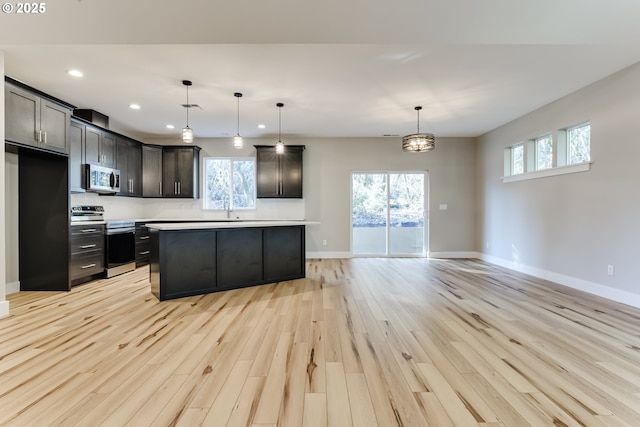 kitchen with pendant lighting, appliances with stainless steel finishes, a kitchen island, plenty of natural light, and light hardwood / wood-style flooring