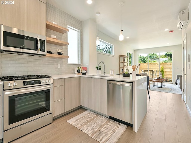 kitchen featuring light brown cabinets, kitchen peninsula, appliances with stainless steel finishes, light hardwood / wood-style flooring, and decorative light fixtures