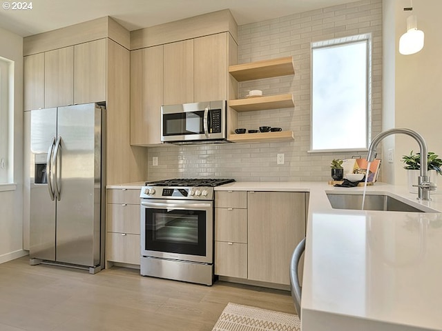 kitchen with appliances with stainless steel finishes, sink, decorative light fixtures, light hardwood / wood-style flooring, and light brown cabinets