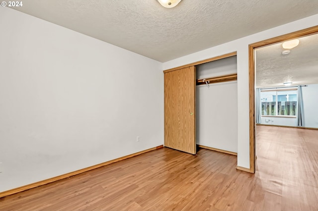 unfurnished bedroom with a textured ceiling, light hardwood / wood-style floors, and a closet