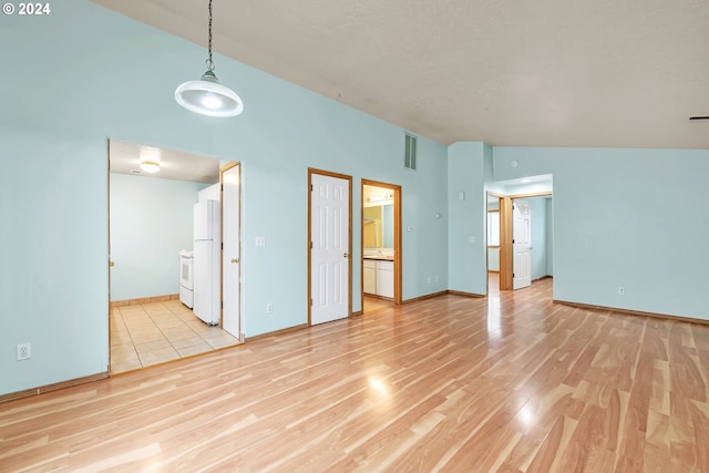 unfurnished bedroom with ensuite bathroom, high vaulted ceiling, white fridge, and light wood-type flooring