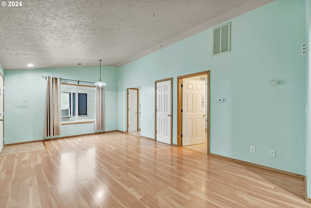 empty room with a textured ceiling, light hardwood / wood-style floors, and lofted ceiling