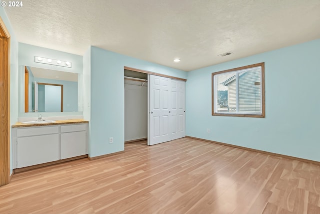 unfurnished bedroom with light hardwood / wood-style flooring, sink, ensuite bathroom, a closet, and a textured ceiling