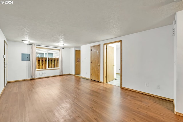 unfurnished living room featuring light hardwood / wood-style flooring, electric panel, and a textured ceiling