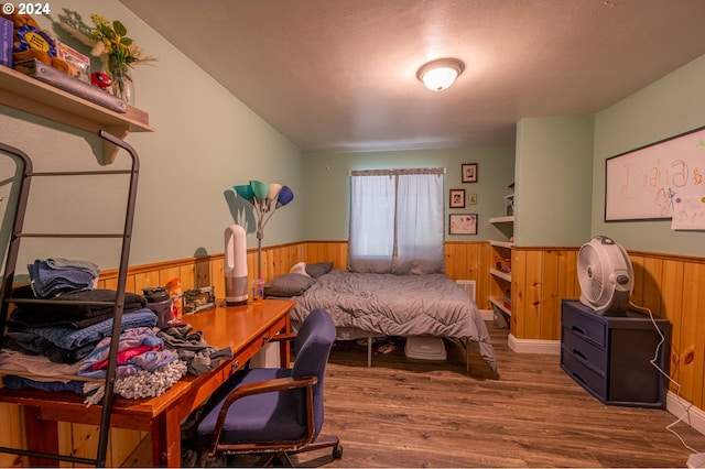 bedroom with a textured ceiling, wood walls, and dark hardwood / wood-style floors