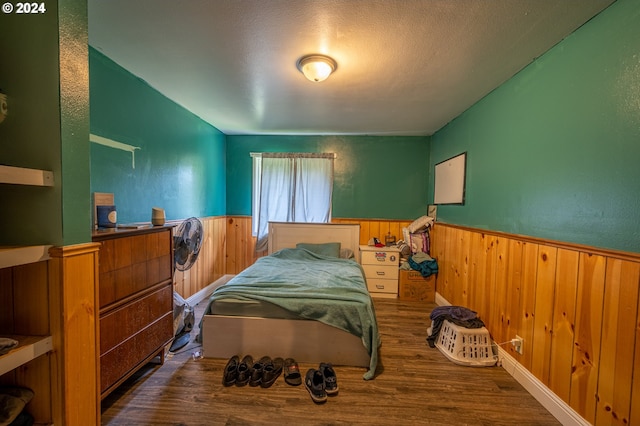 bedroom with hardwood / wood-style floors, wood walls, and a textured ceiling