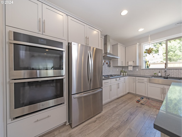 kitchen featuring light hardwood / wood-style floors, white cabinets, backsplash, stainless steel appliances, and wall chimney range hood