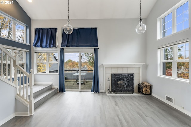 unfurnished living room featuring a tiled fireplace, a healthy amount of sunlight, and hardwood / wood-style flooring