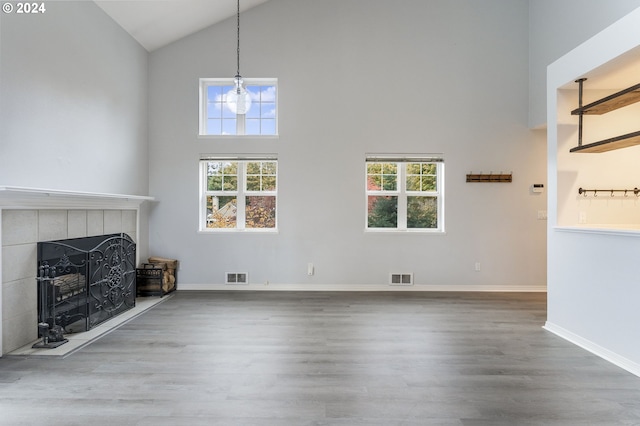 unfurnished living room featuring a tile fireplace, hardwood / wood-style floors, and high vaulted ceiling