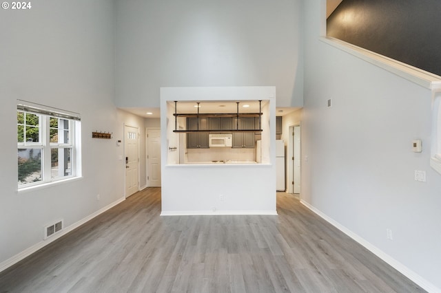 unfurnished living room featuring baseboards, a high ceiling, visible vents, and wood finished floors