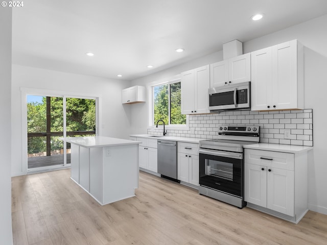 kitchen with light hardwood / wood-style flooring, stainless steel appliances, white cabinets, decorative backsplash, and a center island