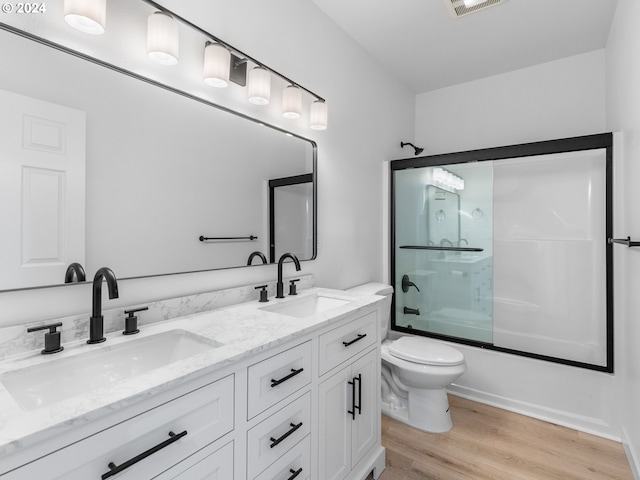 full bathroom with double vanity, hardwood / wood-style flooring, enclosed tub / shower combo, and toilet