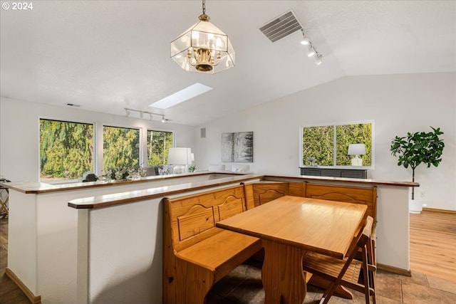 kitchen with decorative light fixtures, rail lighting, lofted ceiling with skylight, an inviting chandelier, and light hardwood / wood-style floors