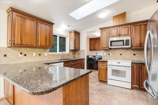 kitchen with vaulted ceiling with skylight, appliances with stainless steel finishes, kitchen peninsula, and washer and dryer