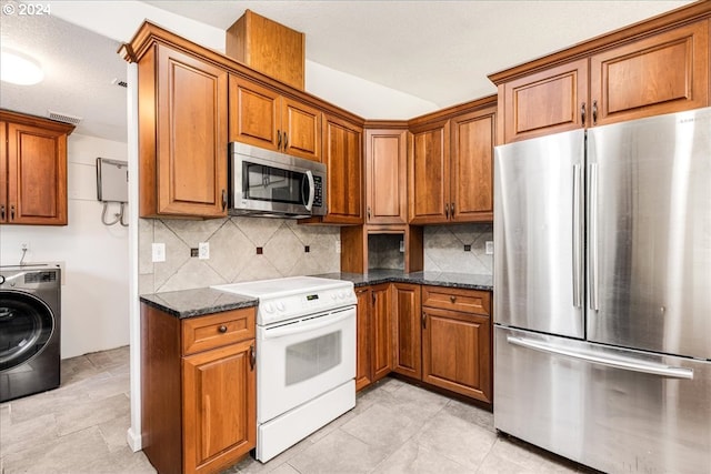 kitchen featuring washer / clothes dryer, dark stone countertops, light tile patterned flooring, backsplash, and stainless steel appliances