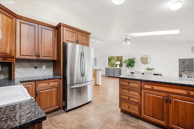 kitchen featuring ceiling fan, light tile patterned flooring, lofted ceiling, stainless steel fridge, and backsplash