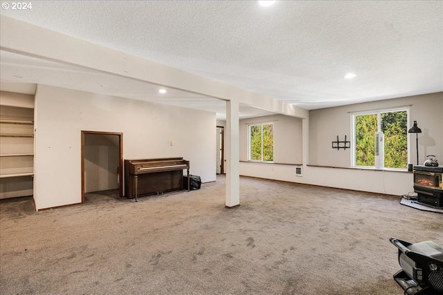 basement featuring a textured ceiling, carpet flooring, and a wood stove