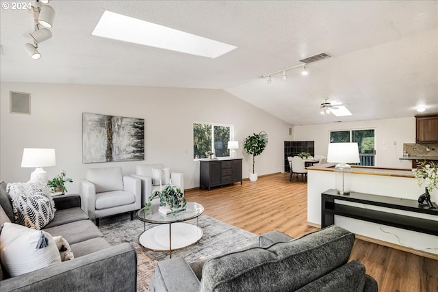 living room with lofted ceiling with skylight, light hardwood / wood-style floors, ceiling fan, and track lighting