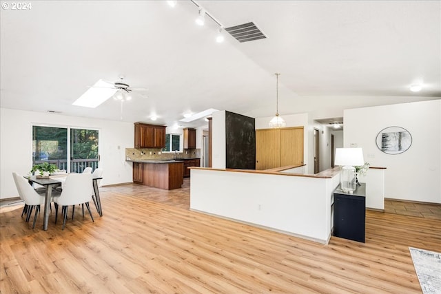 kitchen featuring pendant lighting, light wood-type flooring, kitchen peninsula, and vaulted ceiling with skylight