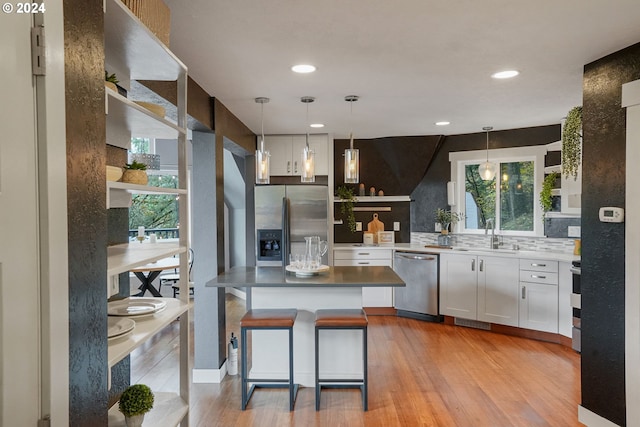 kitchen with appliances with stainless steel finishes, light wood-type flooring, sink, pendant lighting, and white cabinets