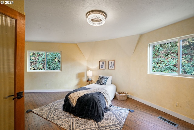 bedroom featuring hardwood / wood-style floors, lofted ceiling, and a textured ceiling