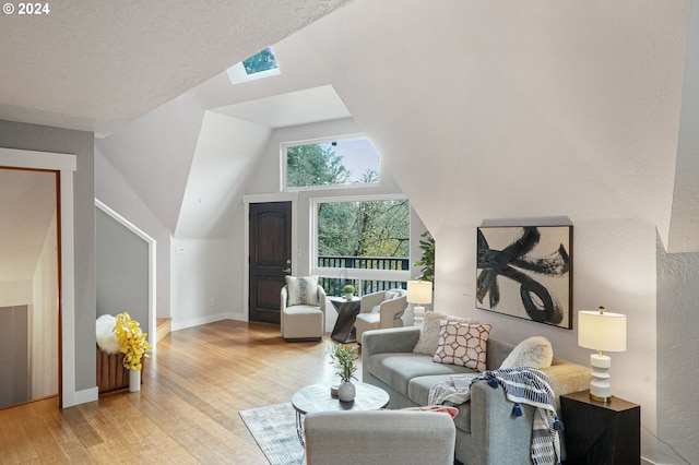 living room featuring vaulted ceiling with skylight, light hardwood / wood-style floors, and a textured ceiling