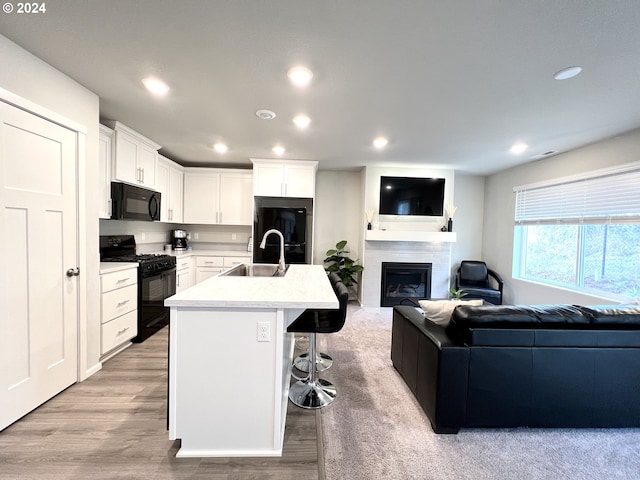 kitchen with a breakfast bar, white cabinetry, a kitchen island with sink, black appliances, and sink