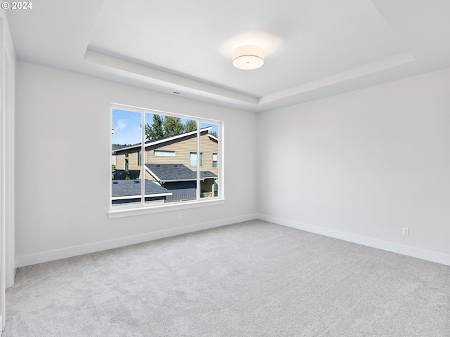 unfurnished room with carpet floors, a tray ceiling, and baseboards